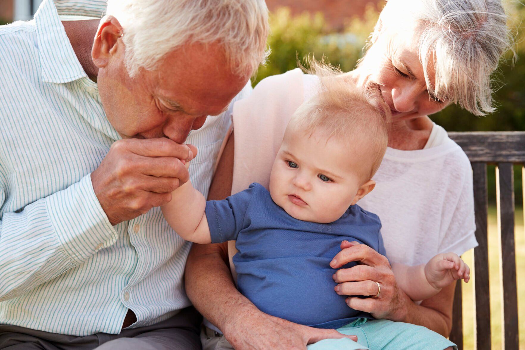 Grandparents Sitting On Seat In Garden With Baby Grandson